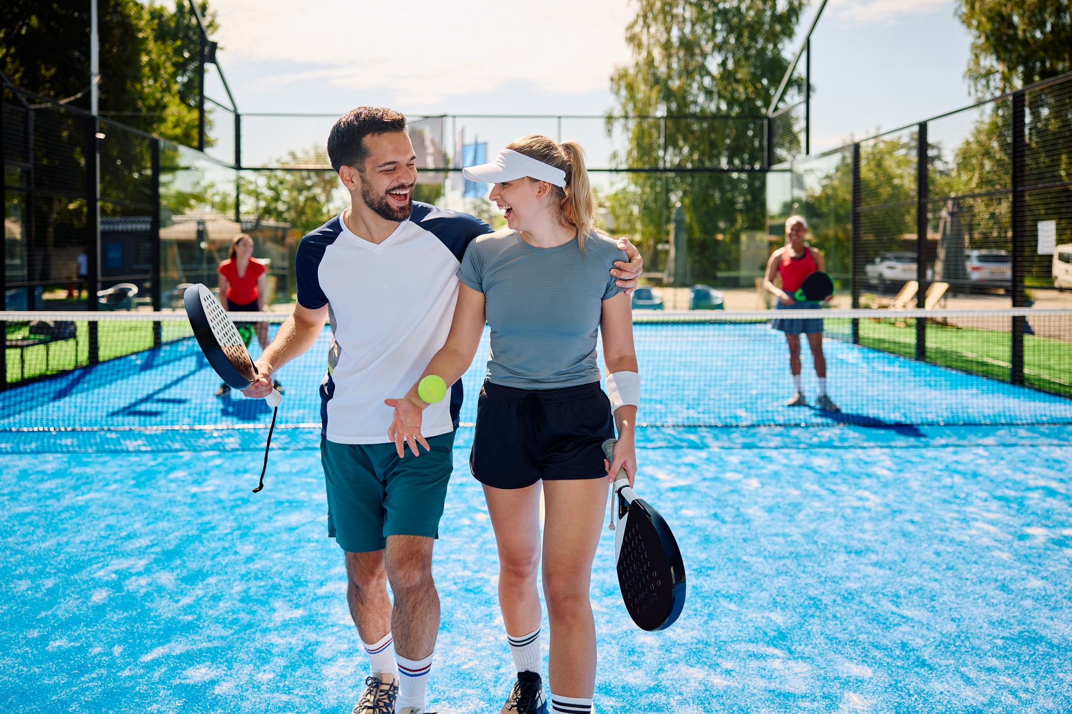 Couple de joueurs de padel souriants avec raquettes et balle